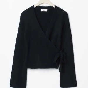 Svart omlottkofta från Gina Tricot XS - Ny skick aldrig andvänd. Mysig svart omlottkofta från Gina Tricot i ullblandning. Koftan har långa ärmar, v-ringning och knytband i sidan för en snygg passform. Perfekt för lager-på-lager och passar till både jeans och kjol.