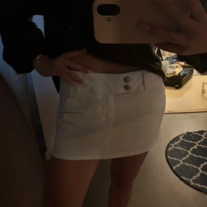 Vit kort jeanskjol med dubbla knappar - Säljer en vit kort jeanskjol med två silvriga knappar i midjan och klassiska fickor fram. Kjolen har en clean och enkel look som är lätt att matcha med olika toppar. Perfekt för dig som gillar en fräsch och stilren vibe. 🤍