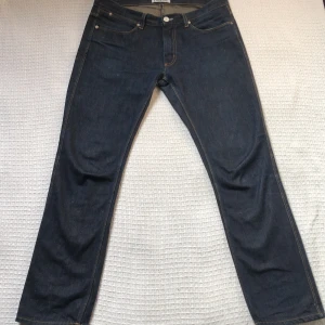 Mörkblå jeans från Acne Studios - Snygga mörkblå jeans från Acne Studios med klassisk femficksdesign och raka ben. Jeansen har kontrastsömmar, dragkedja och knapp med Acne Studios-logga. Tillverkade i robust denim som ger en stilren och tidlös look.