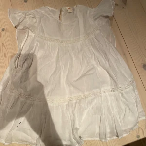 Vit somrig blus från Gina Tricot - Luftig och söt vit blus från Gina Tricot med volangärmar och fina spetsdetaljer. Blusen har en lös passform och är tillverkad i ett tunt, lätt material som passar perfekt för varma dagar.