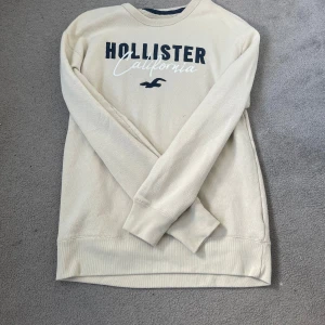 Beige långärmad tröja Hollister - Beige långärmad tröja från Hollister med tryckt logga och texten 'California' på bröstet. Tröjan har rund halsringning och ribbade muddar vid ärmslut och nederkant. Perfekt för en chill och avslappnad stil.