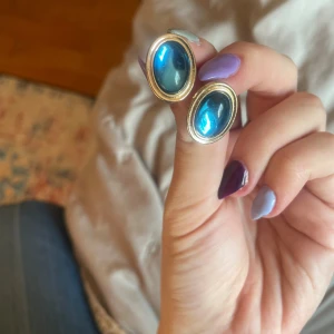 Blå ovala örhängen med guldkant i plast - Säljer ett par snygga örhängen med oval form och en intensivt blå sten i mitten, omgiven av en guldfärgad kant. Retrovibe och helt av plast så inte tunga för öronen! 