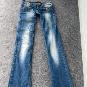 Blåa bootcut jeans från Cross Jeans - Säljer ett par blåa bootcut jeans från berskha Jeans med snygg slitning och kontrastsömmar. Jeansen har klassisk femficksdesign, låg midja och detaljerade bakfickor. Perfekta för dig som gillar en avslappnad och trendig look.