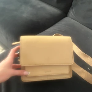 Beige axelväska från DAY ET - Snygg beige axelväska från DAY ET i stilren, fyrkantig modell. Väskan har bred, justerbar axelrem i textil och är tillverkad i slätt skinn. Flera fack inuti, inklusive ett med dragkedja. Perfekt storlek för det viktigaste och enkel att matcha till olika outfits.