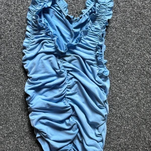 Blå volangbikini med rynkade detaljer - Säljer en ljusblå tröja med volangkant och snygga rynkade detaljer längs hela plagget. Materialet känns mjukt och följsamt mot huden.