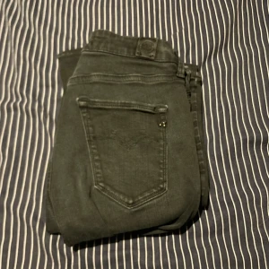 Replay jeans i mörkgrön färg, stl 27/32 - Snygga Replay jeans i mörkgrön färg med klassisk femficksdesign och diskret logga på bakfickan. Jeansen har en slim passform och är tillverkade i mjukt bomullsmaterial med lite stretch för extra komfort. Perfekta för dig som gillar stilrena och bekväma jeans.