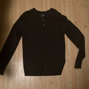 Mörkbrun långärmad tröja från Levi's storlek S - Mörkbrun långärmad tröja från Levi's i standard fit. Tröjan har en rund halsringning och tre knappar framtill. Materialet är bomull med en lätt strukturerad yta som ger en snygg och enkel look. Perfekt till jeans eller chinos.