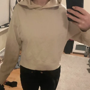 Beige hoodie med huva och lång ärm - Säljer en beige hoodie med croppad passform och huva. Tröjan har långa ärmar och är tillverkad i mjukt bomullsmaterial. Perfekt för chill dagar och enkel att matcha med jeans eller leggings.
