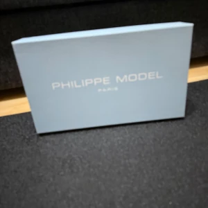 Philippe Model vita sneakers i skinn - Snygga vita sneakers från Philippe Model Paris med klassisk låg profil och rund tå. Skorna har detaljer i beige mocka och svart häl, samt snörning framtill. Tillverkade i skinn och mocka för en lyxig känsla. Kommer med originalkartong, dustbag och taggar.