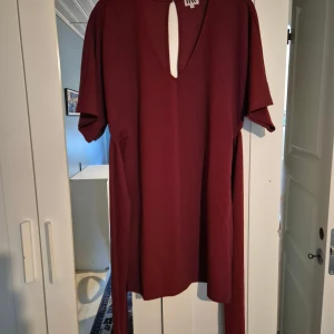 Vinröd klänning från Make Way - Snygg vinröd klänning från Make Way med v-ringning och korta ärmar. Modellen är rak och har ett tillhörande bälte i midjan för extra stilpoäng. Perfekt för dig som gillar enkel men trendig design.