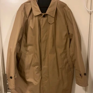 Beige rock från GANT i storlek 3XL - Snygg beige rock från GANT i storlek 3XL. Jackan har klassisk krage, knäppning framtill och två fickor på sidorna. Insidan är fodrad i mörkblått tyg. Perfekt för dig som vill ha en stilren och tidlös look.