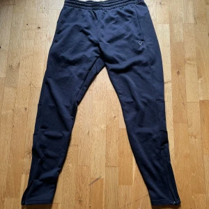 Svarta mjukisbyxor från SOC - Svarta mjukisbyxor från SOC med elastisk midja och dragsko. Byxorna har smal passform, diskret logga på höften och är tillverkade i mjukt bomullsmaterial. Perfekta för chill eller träning, med dragkedja vid benslut för extra komfort.