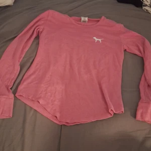 Victoria secret tröja - Rosa långärmad tröja från PINK by Victoria's Secret med vit hundlogga på bröstet och stor hundsilhuett på ryggen. Mjuk och skön i bomullsmix, perfekt för chill dagar. Rund halsringning och avslappnad passform.