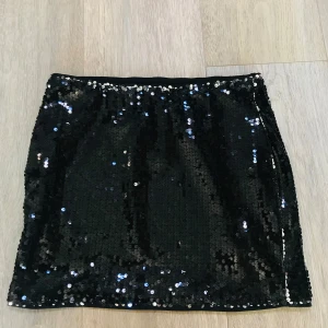 Svart paljettkjol - Snygg svart kortkjol täckt med glittriga paljetter. Kjolen har en rak passform och är perfekt då den inte sticks!                                                Köptes på Plick men säljer vidare för den inte passade.