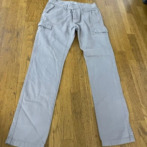 Grå cargopants med raka ben - Snygga grå cargopants med raka ben och flera praktiska fickor på sidorna. Byxorna har bälteshällor, knapp och dragkedja i midjan. Tillverkade i mjuk bomull som är skön att ha på sig. Perfekt för dig som gillar en avslappnad och funktionell stil.