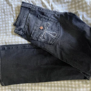 Svarta jeans med broderade bakfickor - Snygga svarta jeans från Cross med coola broderade detaljer på bakfickorna och kontrastsömmar. Klassisk femficksmodell med knapp och dragkedja fram. Jeansen har en rak passform och har en bekväm känsla. Knappt använda. 