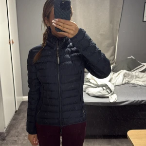 Svart lättviktsdunjacka Parajumpers XS - Säljer en svart, superlätt dunjacka från Parajumpers i storlek XS. Jackan har quiltad design, hög krage och dragkedja framtill. Perfekt för dig som vill ha en smidig och snygg jacka med sportig känsla. Fickor med dragkedja och innerficka med säkerhetsmärkning.