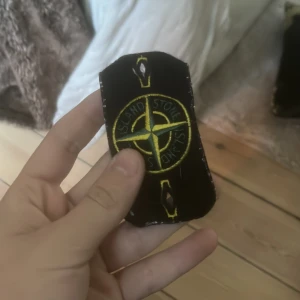 Stone Island badge svart/gul - Säljer en klassisk svart Stone Island badge med broderad kompasslogga i gult och grönt. Perfekt att fästa på jackor eller tröjor för att ge din outfit en streetwear vibe.