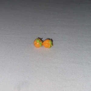 Söta örhängen med apelsinmotiv - Små och färgglada örhängen formade som apelsiner med orange frukt och gröna blad. Perfekta för dig som vill ha en lekfull och unik detalj till din stil. Säljs som ett par.