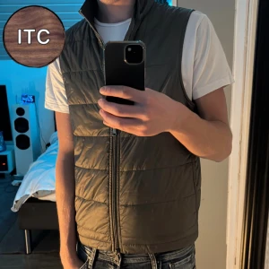 Olivgrön väst  - Snygg olivgrön quiltad dunväst med hög krage och dragkedja framtill. Västen har en stilren look och passar perfekt över en t-shirt eller hoodie. Enkel och clean design som är lätt att matcha.