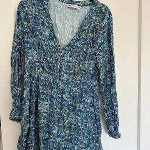 Blåmönstrad kortklänning från Zara - Supersnygg, populär, slutsåld blå och vit kortklänning från Zara med v-ringning och långa ärmar. Klänningen har ett unikt mönster i olika blå toner och en lätt, flowy passform. Perfekt för dig som gillar färg och mönster! 💙