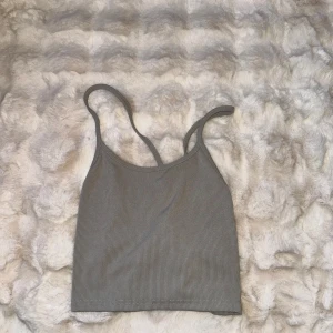 Grå ribbad linnetopp med snörning - Snygg grå ribbad linnetopp med smala axelband och snörning i ryggen. Toppen är croppad och har en enkel, stilren design som passar perfekt till jeans eller kjol. Materialet är mjukt och stretchigt för en bekväm passform.
