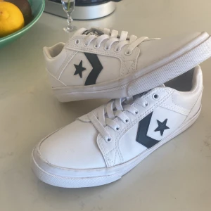 Vita Converse All Star sneakers - Säljer ett par vita Converse All Star sneakers med svart stjärnlogga på sidan. Skorna har klassisk snörning, rund tå och platt sula. Tillverkade i syntetmaterial med stilren design som passar till det mesta. Perfekta för dig som gillar en clean och sportig look. Dem är helt oanvända men testade i butik. 