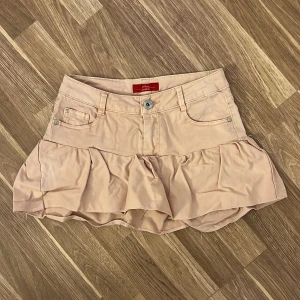 Ljusrosa volangkjol med jeanslook - Supersöt beige kortkjol från s.Oliver med volang nertill och klassiska jeansdetaljer som fickor och bälteshällor. Kjolen har en feminin och lekfull stil, perfekt för dig som gillar en trendig och avslappnad look.