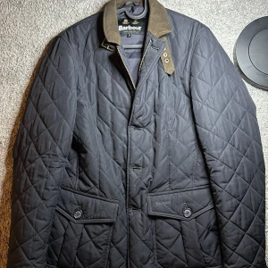 Svart quiltad jacka från Barbour S - Quiltad marin blå jacka från Barbour i storlek S. Klassisk modell med bruna detaljer på kragen, två stora fickor framtill med knappar och dragkedja. Jackan har lång ärm och snyggt rutmönster i tyget. Perfekt för höst och vår. Jag köpte den för 3,200kr, använd en vinter. Inga skador eller något konstigt. Precis som på bilderna. Passar om du är 168-175. Den är för liten på mig och jag är 176 ungefär normal vikt.