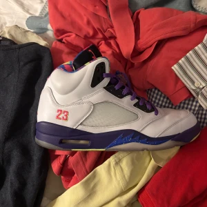 Nike Air Jordan 5 'Bel-Air' sneakers - Nike Air Jordan 5 'Bel-Air' med vit ovandel i skinn, lila snörning och sula, samt färgglada detaljer på plösen och innertyget. Snygg 23-brodyr på sidan och ikonisk Jumpman-logga. Perfekta för dig som vill sticka ut med en retro vibe och cool färgkombo.