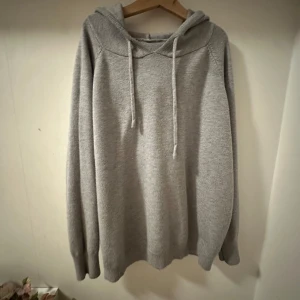 Merinoull hoodie - Mysig grå hoodie med huva och snörning framtill. Tröjan har lång ärm och ribbade muddar vid ärmslut och nederkant. Perfekt för chill dagar eller när du vill vara extra bekväm.