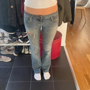 Lågmidjade bootcut jeans från Pinko - Säljer ett par ljusblå lågmidjade jeans från Pinko med bootcut passform. Jeansen har slitningar och hål på ena låret. de är lite slitna vid bakfickorna och gylfen är trasig, men de är inget man tänker på då den är så kort!! därav priset