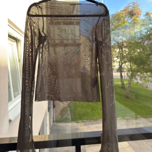 Brun mesh topp med strassdetaljer från weekday - Säljer en transparent brun mesh topp med långa ärmar och snygga strassdetaljer i abstrakta mönster över hela plagget. Toppens material är tunn och stretchig syntet, finns en slits längst ner vid ärmarna och har en rak urringning. Köpt för 499kr