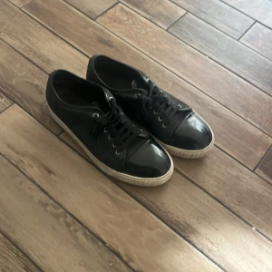 Svarta Lanvins Snabb affär - Snygga svarta sneakers från Lanvin med klassisk design. Skorna har snörning, rund tå och en kontrasterande vit sula. Ovandelen är i strukturerat skinn och tån är i blankt material för en stilren look. Perfekta för dig som gillar exklusiva och tidlösa sneakers. SNABB AFFÄR