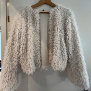 Vit fluffig pälsjacka från Lindex - Supermjuk och fluffig vit pälsjacka från Lindex i storlek 170. Jackan har lång ärm, öppen framtill och går även att stänga med tre stycken knappar. 
