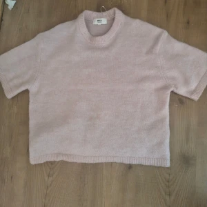 Ljusrosa stickad tröja Gina Tricot - Supermjuk ljusrosa stickad tröja från Gina Tricot i ullblandning. Tröjan har korta ärmar, rund halsringning och ribbade kanter. Perfekt för lager-på-lager och chill vibes.använd några gånger 