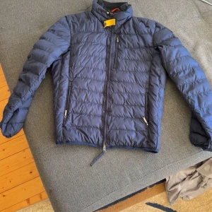 Blå dunjacka från Parajumpers L eller byte  - Säljer en blå dunjacka från Parajumpers i storlek L. Jackan är superlätt, har quiltad design, dragkedja framtill och flera fickor. Insidan är ljusbeige och jackan har en snygg patch på ärmen. Perfekt för kyliga dagar och riktigt stilren. Priset kan diskuteras