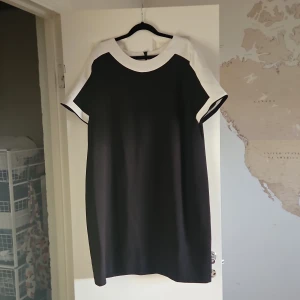 Svartvit klänning Dorothy Perkins - Snygg svart klänning från Dorothy Perkins med vita detaljer vid halsringning och ärmslut. Rak passform och kort ärm, perfekt för dig som gillar enkel och stilren design. Dragkedja bak för enkel påklädning. Storlek EU 48.