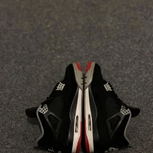 Nike Air Jordan 4 Black/Red - Säljer ett par Nike Air Jordan 4 i svart med röda och grå detaljer. Skorna har klassisk meshpanel, snörning och den ikoniska Jumpman-loggan på plösen. Snygg kontrast mellan svart mocka och gråa samt röda inslag på sulan. Perfekta för dig som gillar streetwear och sneakers med attityd.