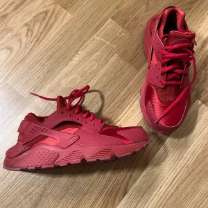 Nike Air Huarache helröda sneakers - Nike Air Huarache sneakers i helrött med cool design och chunky sula. Skorna har snörning, rund tå och är tillverkade i en mix av syntet och textil. Perfekta för dig som vill sticka ut med en färgstark look och maximal komfort.