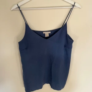 Mörkblå linnetopp med smala axelband - Säljer en stilren mörkblå linnetopp från H&M med smala axelband och v-ringning både fram. Materialet är svalt och lätt, vilket gör den superbekväm att bära. Avklippt för att matcha snyggt med jeans 