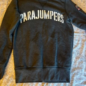 Mörkgrå sweatshirt från Parajumpers - Snygg mörkgrå sweatshirt från Parajumpers med stort vitt tryck över bröstet. Klassisk rund halsringning och långa ärmar. Perfekt för dig som gillar stilrena och sportiga plagg med tydlig logga.