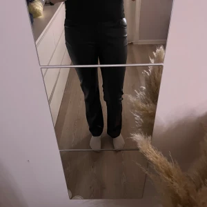 Svarta raka byxor i skinnimitation - Snygga svarta skinnbyxor med rak passform. De har klassisk midja och stilrena fickor både fram och bak. Perfekta för dig som vill ha en cool och trendig look med lite edge.