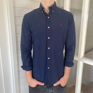 Ralph lauren skjorta - Säljer denna riktigt snygga mörkblåa Ralph lauren skjorta! Den är i mycket bra skick utan några defekter, storlek M modell slim fit, den är 77 cm lång och 50 cm bred under armhålorna, jag på bilderna är 184 cm och väger 80 kg, hör gärna av dig vid frågor!