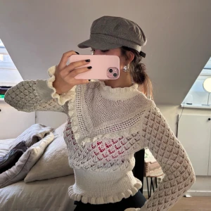 Vit stickad blus med volangdetaljer - Superfin vit stickad blus med volangdetaljer vid hals, ärmslut och nederkant. Genombrutet mönster och hög krage. Perfekt för dig som gillar unika och söta plagg med mycket detaljer. Använd fåtal gånger