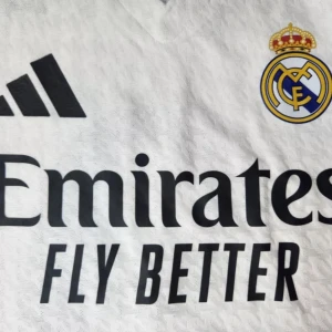 Real Madrid Mbappé 9 Adidas matchtröja - Real Madrid hemmatröja med Mbappé och nummer 9 på ryggen. Vit med subtilt mönster, klubbmärke och Adidas-logga på bröstet samt sponsortryck. Tillverkad i lätt funktionsmaterial (HEAT.RDY) för bästa komfort på planen.