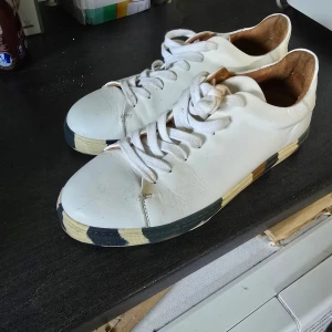 Vita sneakers med färgad sula - Snygga vita sneakers med snörning och cool randig sula i svart, beige och grått. Skorna har rund tå och är tillverkade i skinn med brunt innerfoder. Perfekta för dig som vill ha en stilren men unik look.