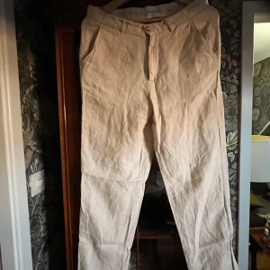 Beiga linnebyxor med rak passform - Snygga beiga linnebyxor med rak passform och klassisk design. Byxorna har fickor i sidorna och stängs med dragkedja och knapp. Perfekta för en avslappnad och stilren look under varmare dagar.