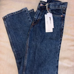 Mörkblå straight jeans från Gina Tricot - Mörkblå jeans från Gina Tricot med rak passform och klassisk femficksdesign. Byxorna har hög midja, silverfärgad knapp och dragkedja. Tillverkade i robust denim med snygga kontrastsömmar. Perfekta för en clean och tidlös look. Nypris:499kr.