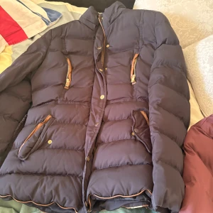 Fyra trendiga jackor i vinröda och mörka toner - Säljer fyra jackor: en är mörkblå pufferjacka med bruna detaljer och dragkedjor, en vinröd ärmlös pufferjacka med dragkedja, en quiltad vinröd rock från Belstaff med bälte och knappar, samt en vinröd dunjacka med huva och svarta detaljer. Perfekta för höst och vinter!